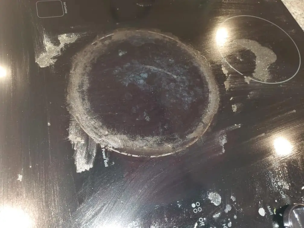 Close-up of baked-on grease rings on a glass stovetop burner before degreasing