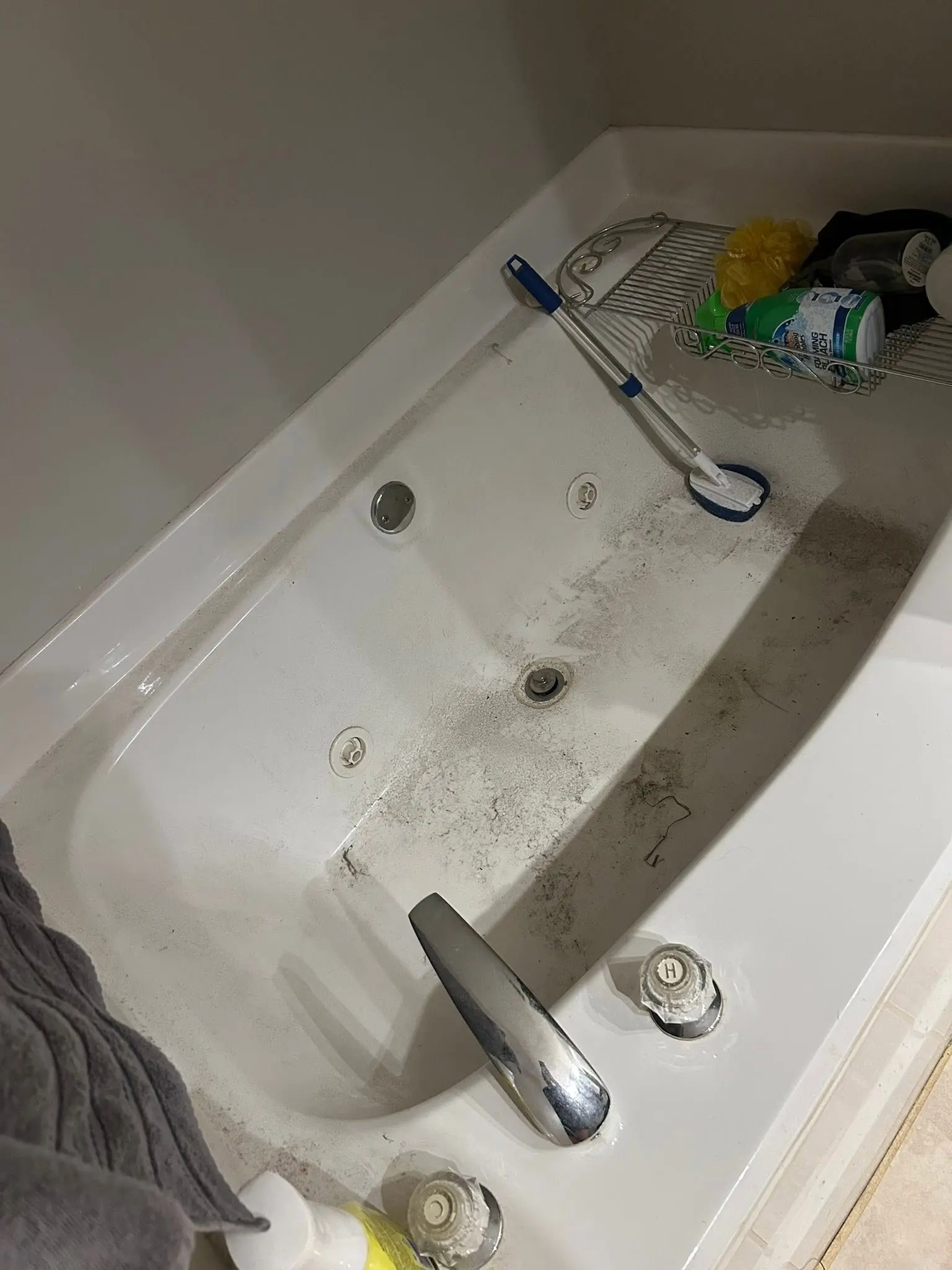 Jetted tub with hard water grime and dust along the ledge before deep cleaning
