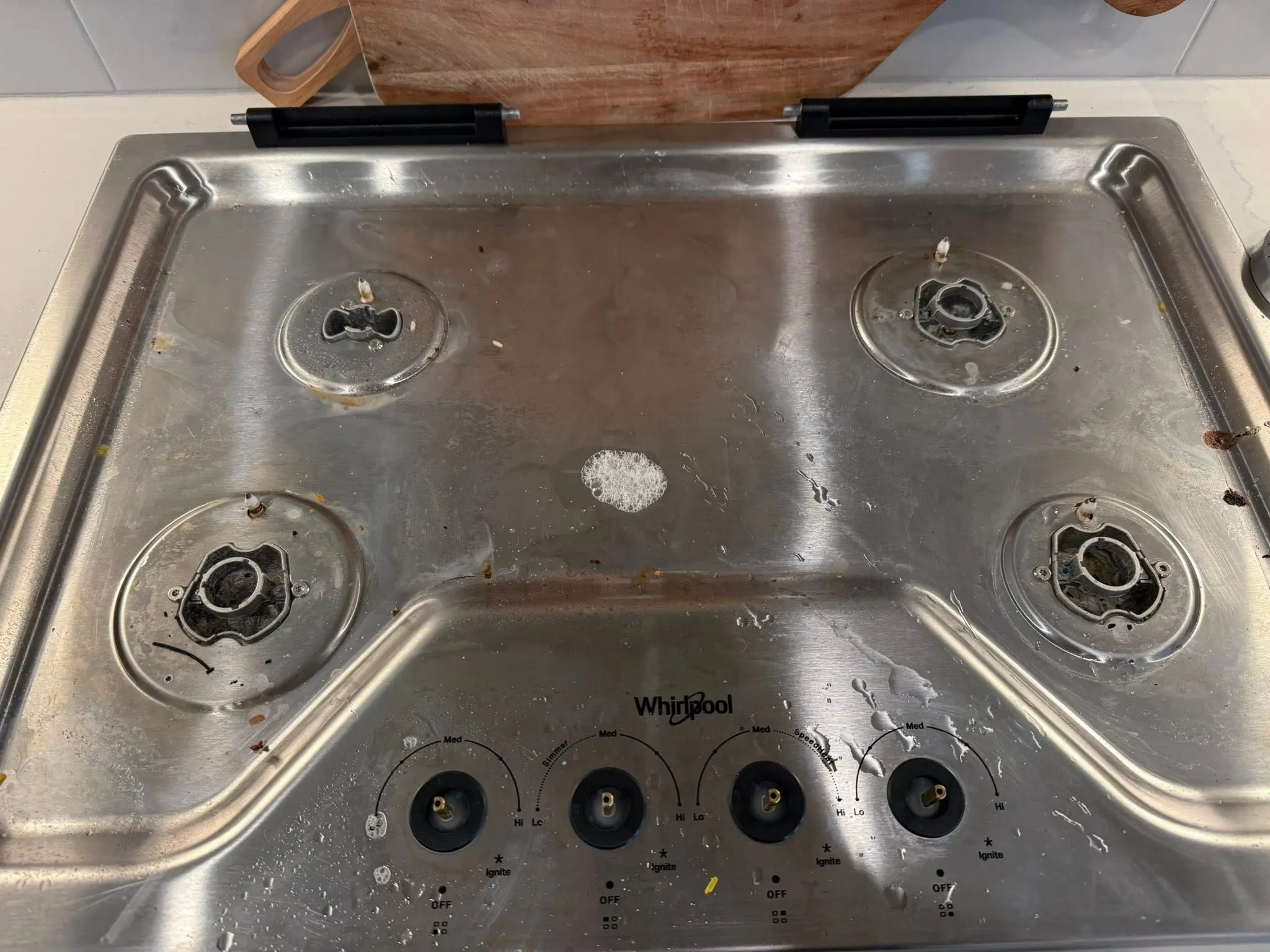 Stainless steel gas cooktop with grease and crumbs around the burners before cleaning