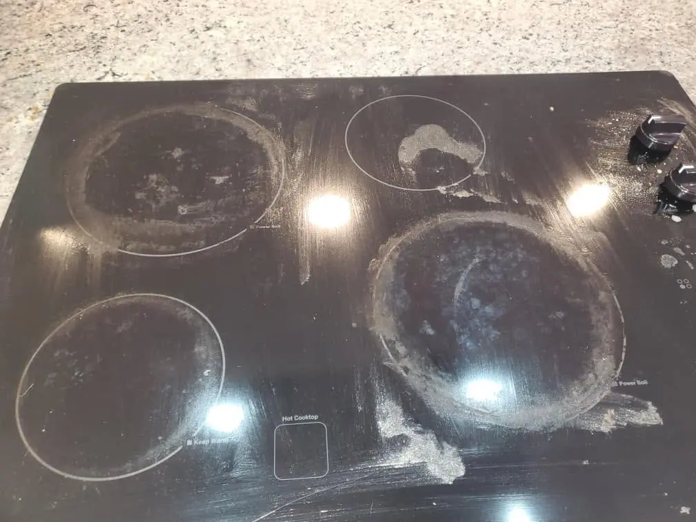 Black glass cooktop covered in burnt-on food residue before appliance detailing